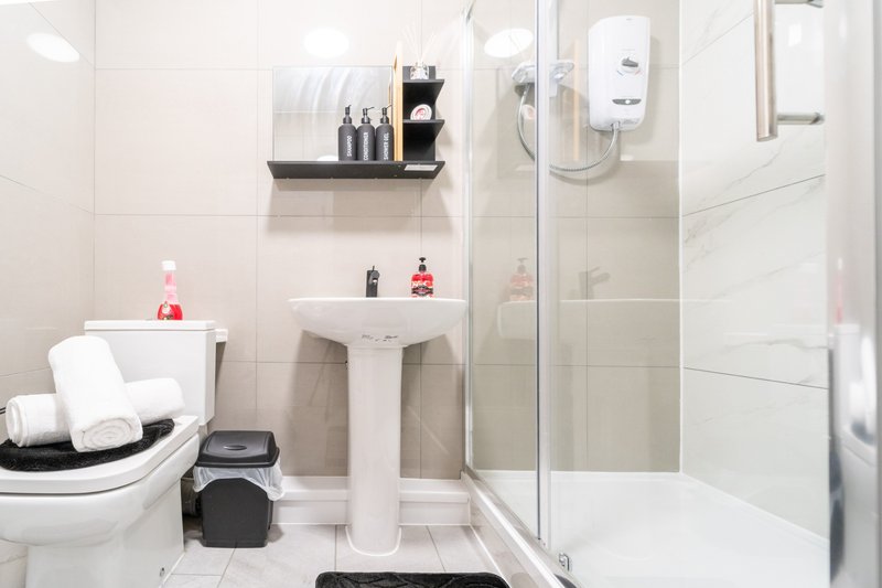 Modern bathroom with white tile, pedestal sink, toilet, shower enclosure and shelving