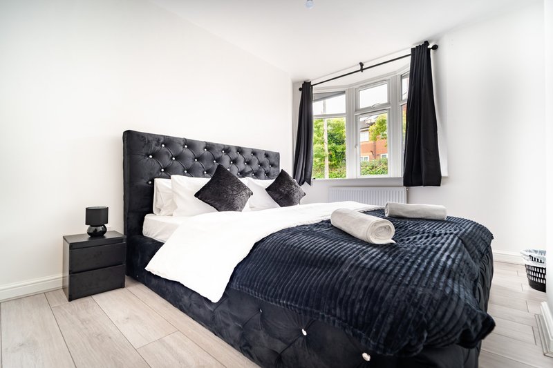 Modern bedroom with upholstered bed, white bedding, dark pillows and throw blanket