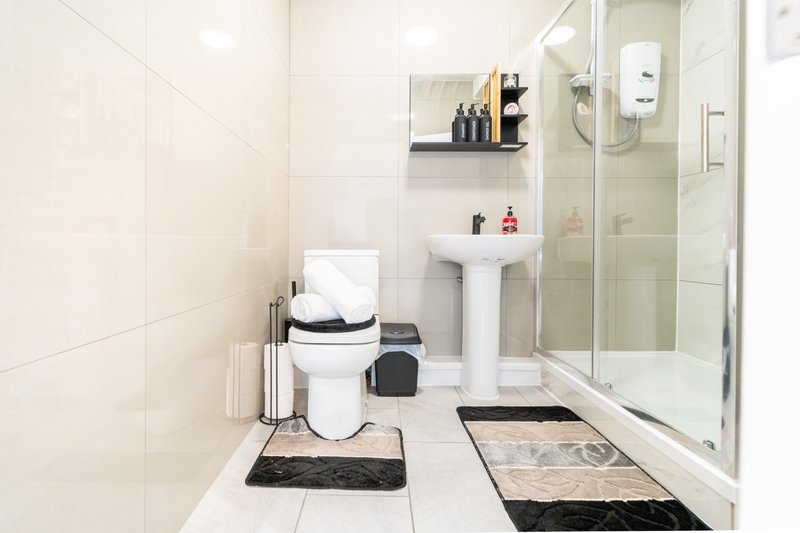 Clean modern bathroom with white toilet, pedestal sink, glass shower enclosure and tiled floor