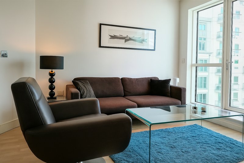 Modern living room with dark leather armchair, brown sofa, glass table, blue rug and city view
