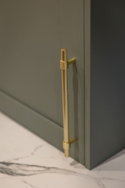 Close-up of gold cabinet handle on sage green cabinetry with marble flooring