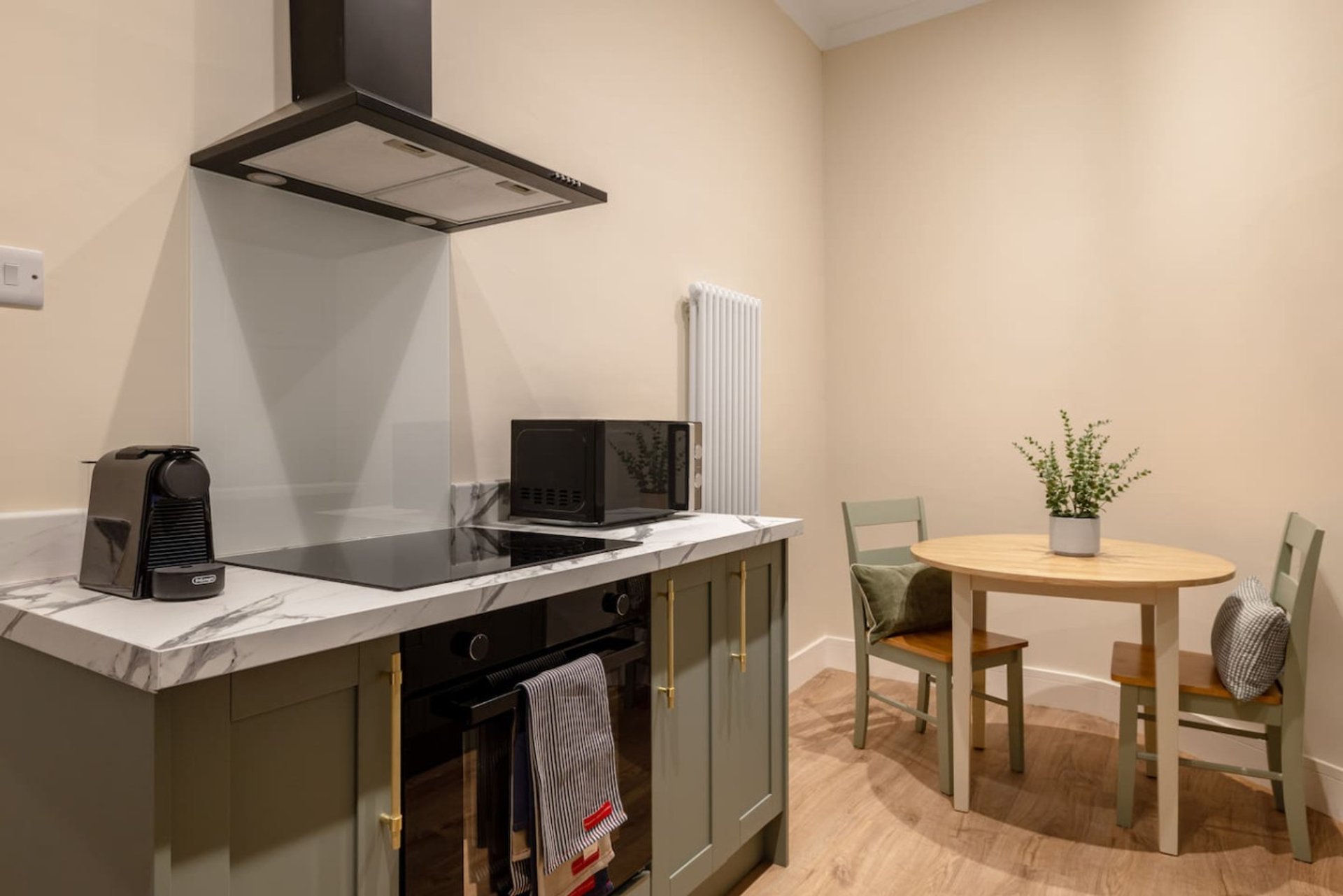 Open-plan kitchen and dining area with olive cabinetry, range hood, dining table and chairs