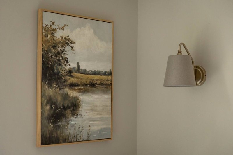 Bedroom wall with framed landscape painting and wall-mounted sconce lamp