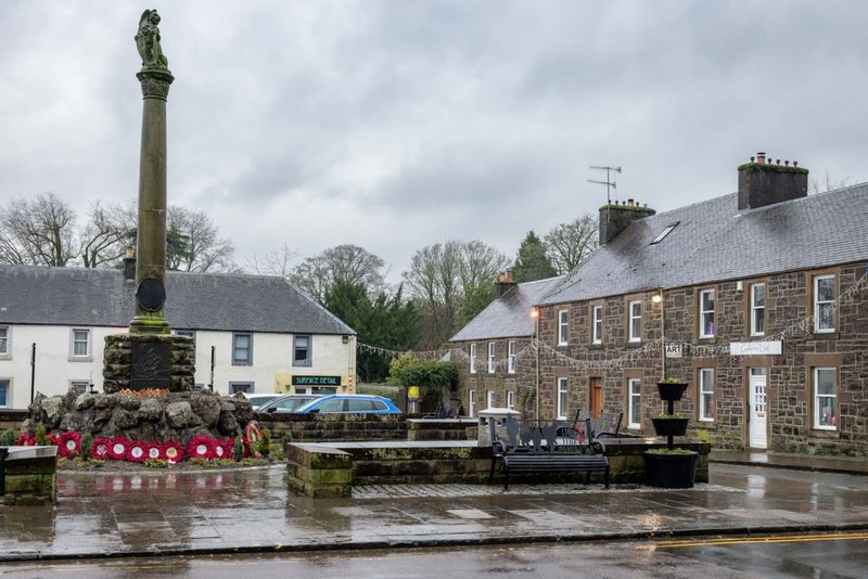 Waterside stone buildings with monument and flowering planters beside canal