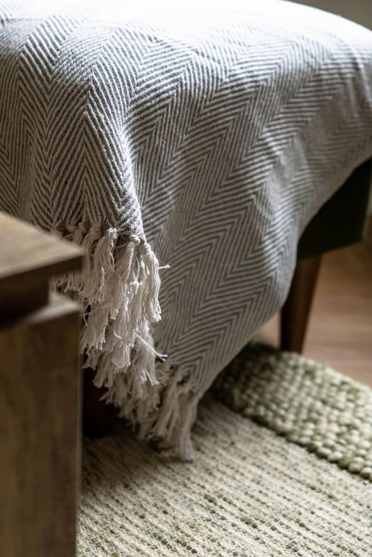Bed with gray herringbone throw blanket and green woven area rug