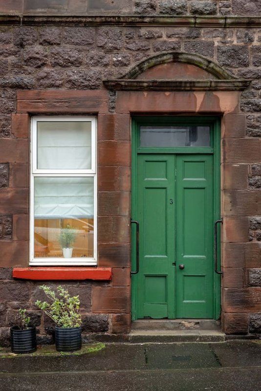 Red brick terraced house exterior with green door, white window and potted plants