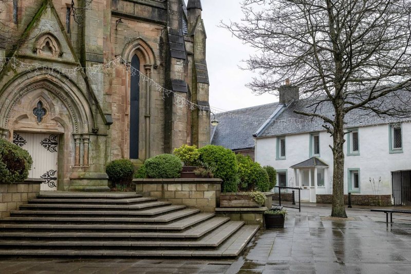 Stone church with Gothic architecture and adjoining white residential building, wet paving