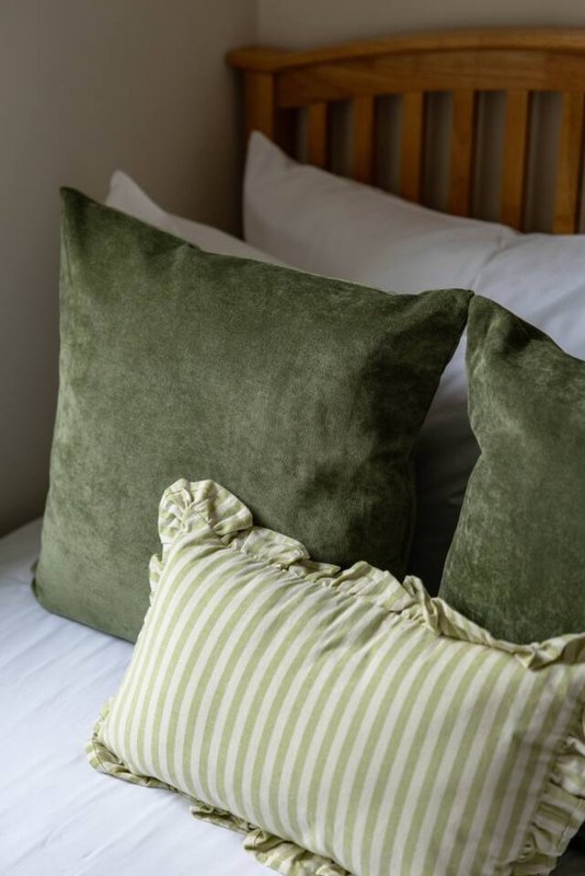 Wooden bed with green and striped cushions and white pillows