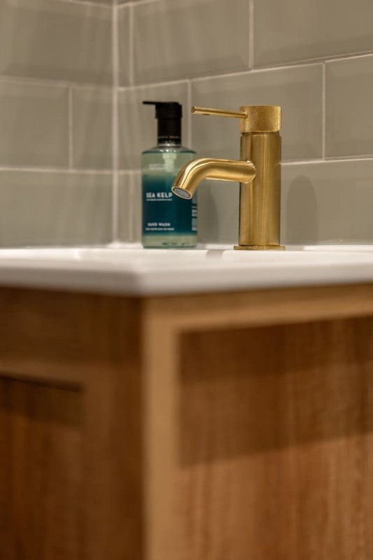 Bathroom sink with gold faucet, soap dispenser, and toiletries on white counter