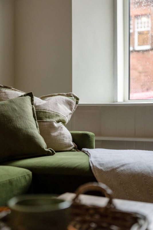 Living room with green sofa, cushions, and window overlooking brick building