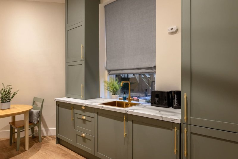 Modern kitchen with olive-green cabinetry, marble countertop, brass fixtures and backsplash