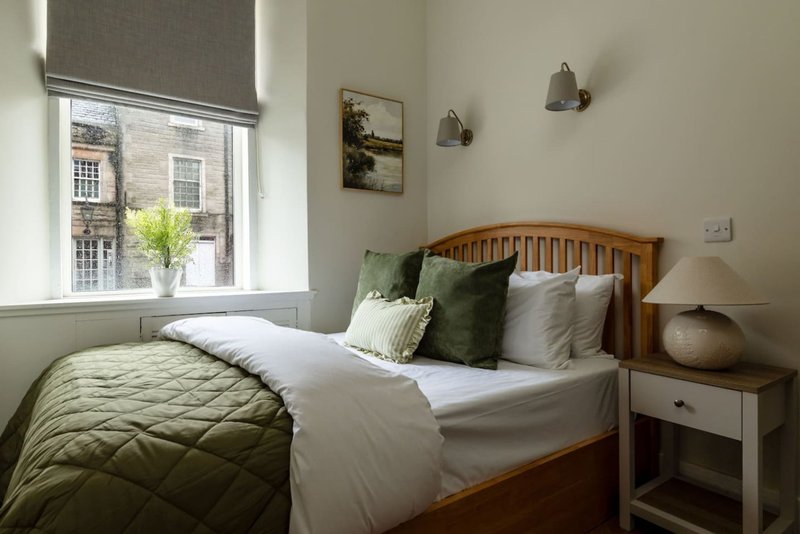 Bedroom with wooden bed, white and green bedding, nightstand, pendant lights and window view