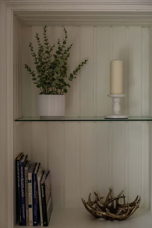 White shelving unit with potted plant, candle, books and decorative wooden bowl