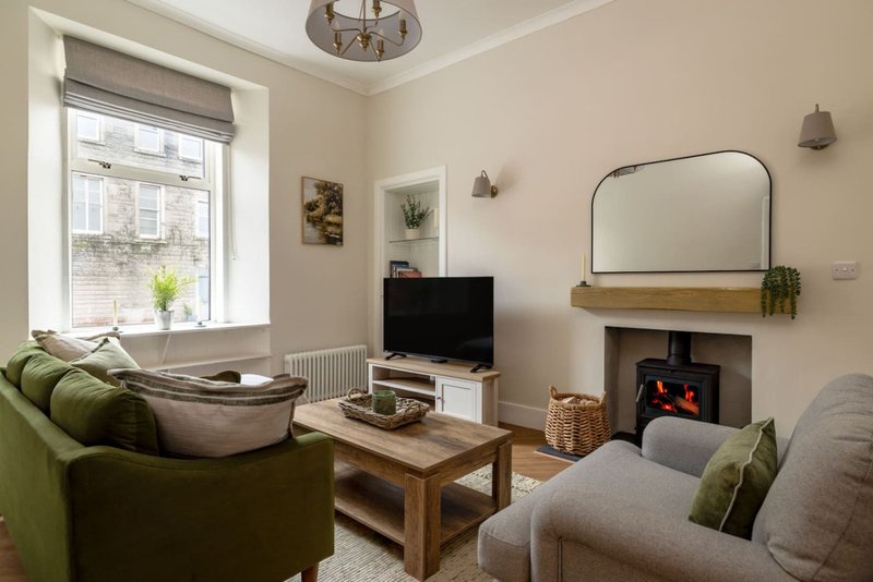 Bright living room with green armchair, grey sofa, fireplace, TV, wooden coffee table and arched mirror