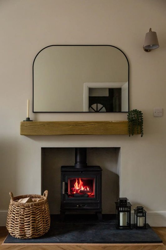 Fireplace with black stove, wooden mantle, rounded mirror, woven basket, and decorative items