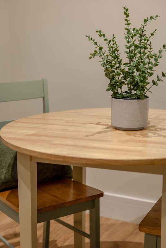 Round wooden dining table with green chairs and potted plant centerpiece