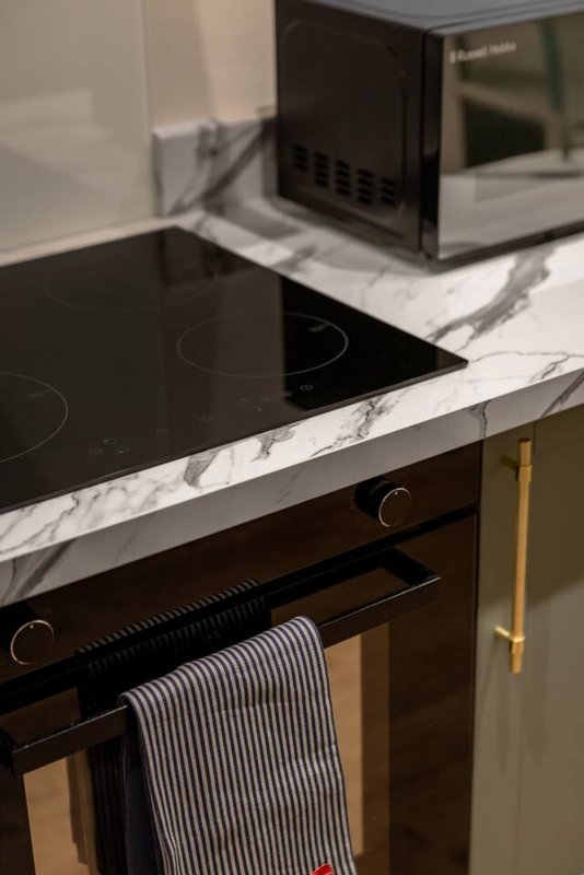 Modern kitchen with black induction cooktop, marble countertop, microwave and gold handles