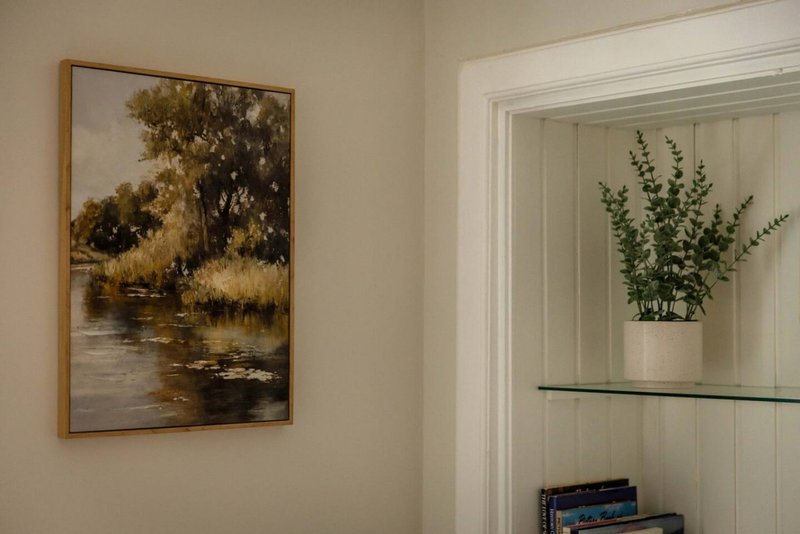 Hallway corner with framed landscape artwork on wall and built-in shelving with potted plant