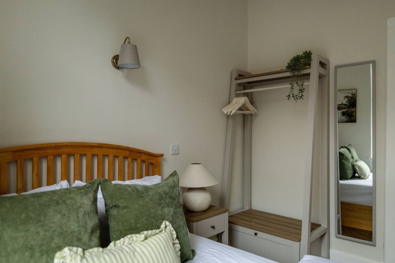 Bedroom with wooden bed frame, green pillows, bedside lamp and wardrobe
