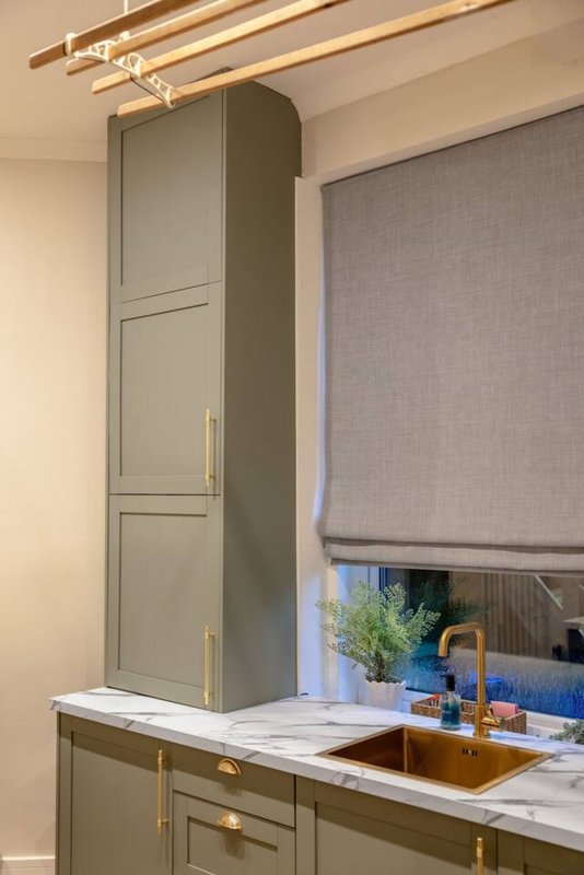 Modern kitchen with olive-green cabinetry, marble countertop, copper sink fixture and brass hardware