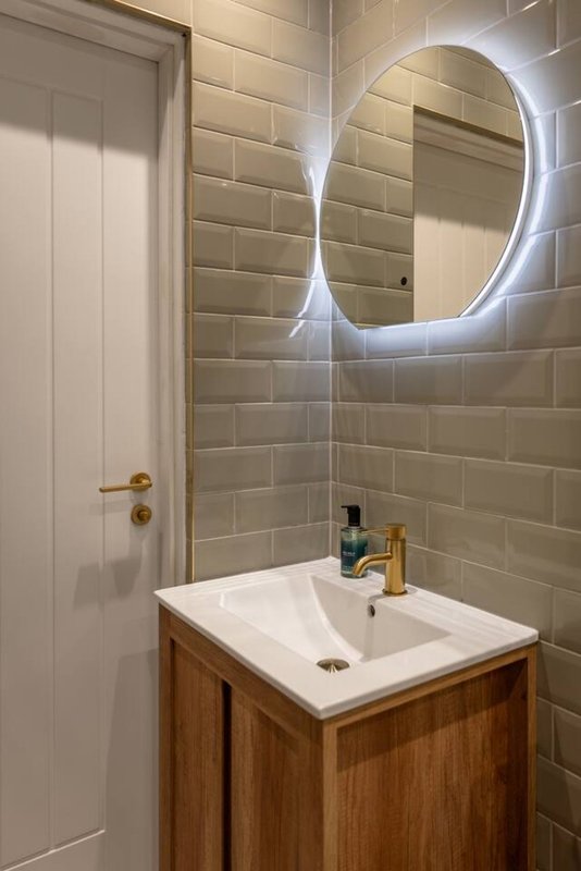 Modern bathroom with illuminated oval mirror, white sink, wooden vanity and beige subway tile