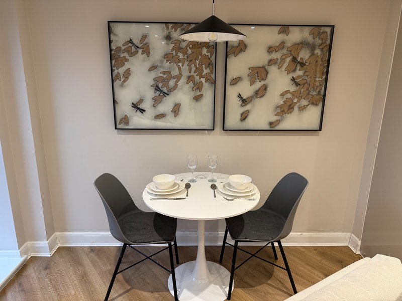 Small dining area with round white table, two black chairs, place settings, and framed wall art above