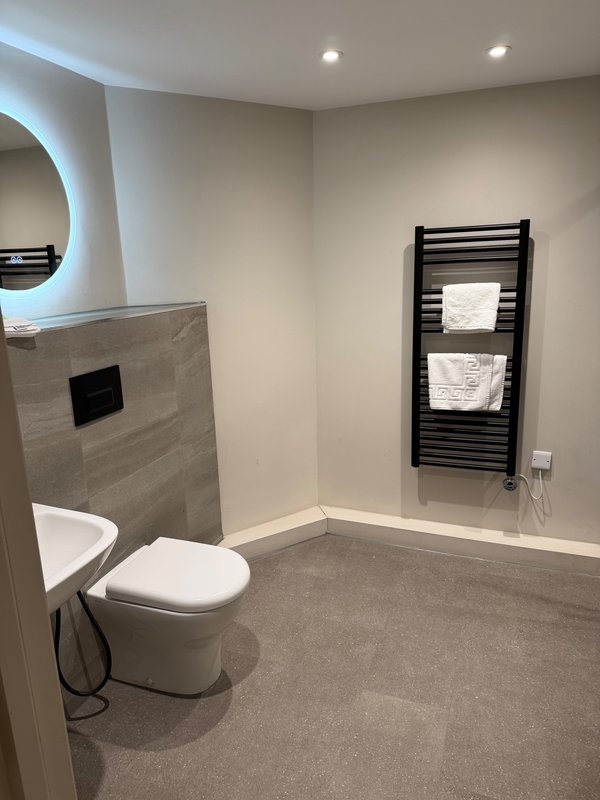 Modern bathroom with toilet, heated towel rail, circular mirror and recessed lighting