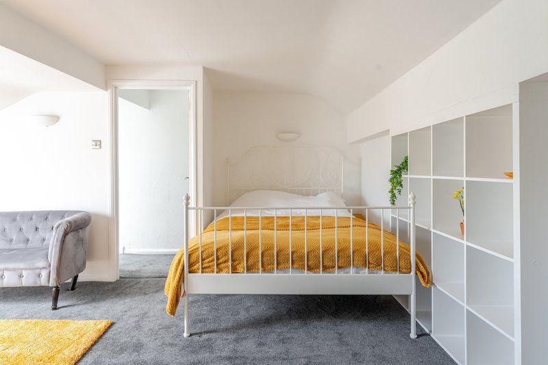 Bright bedroom with metal-frame bed, yellow bedding, grey carpet, white storage shelving and upholstered chair