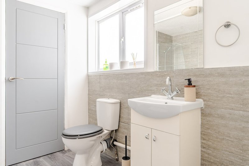 Modern bathroom with white toilet, wall-mounted sink, vanity storage, and window with natural light
