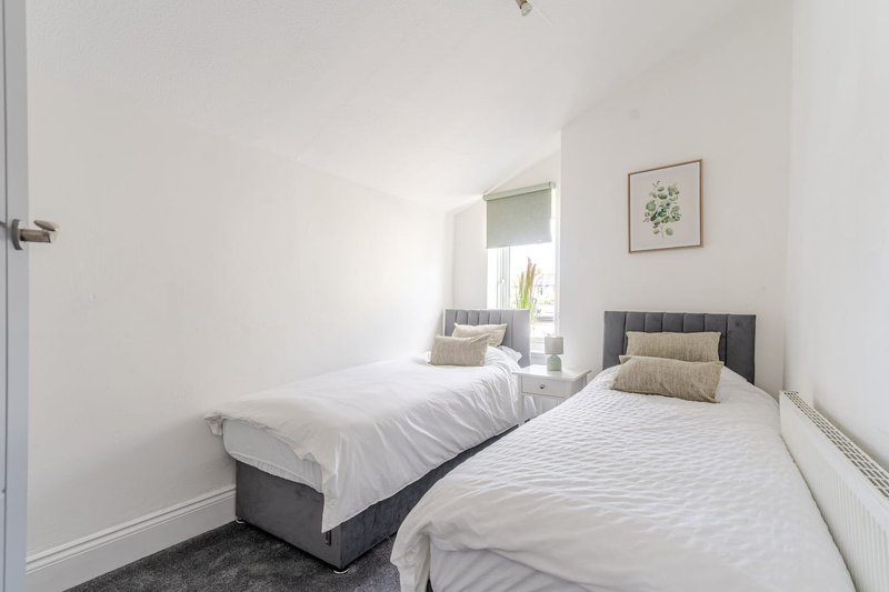 Bright twin bedroom with two single beds, white bedding, mirror, and botanical wall art