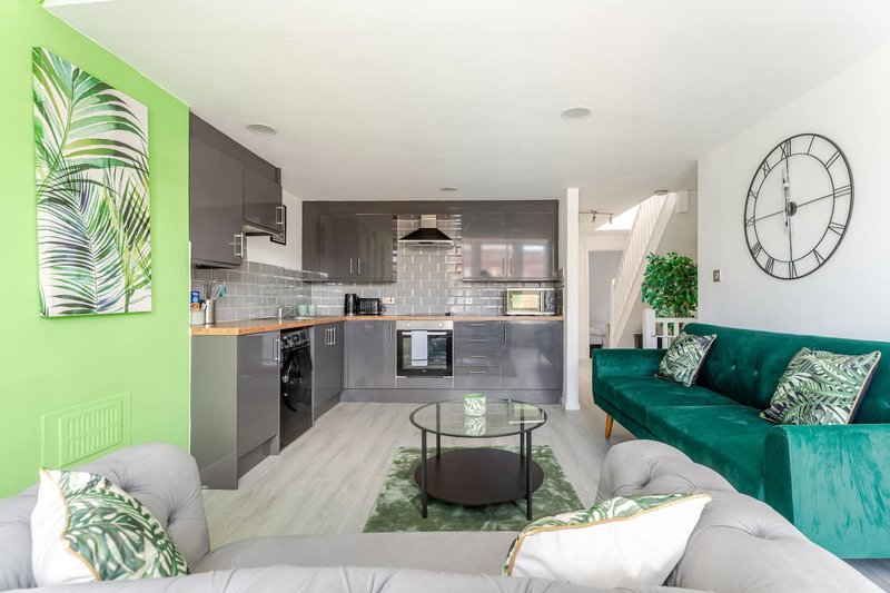 Open-plan living area with kitchen, dining table, and teal sofa with green accents