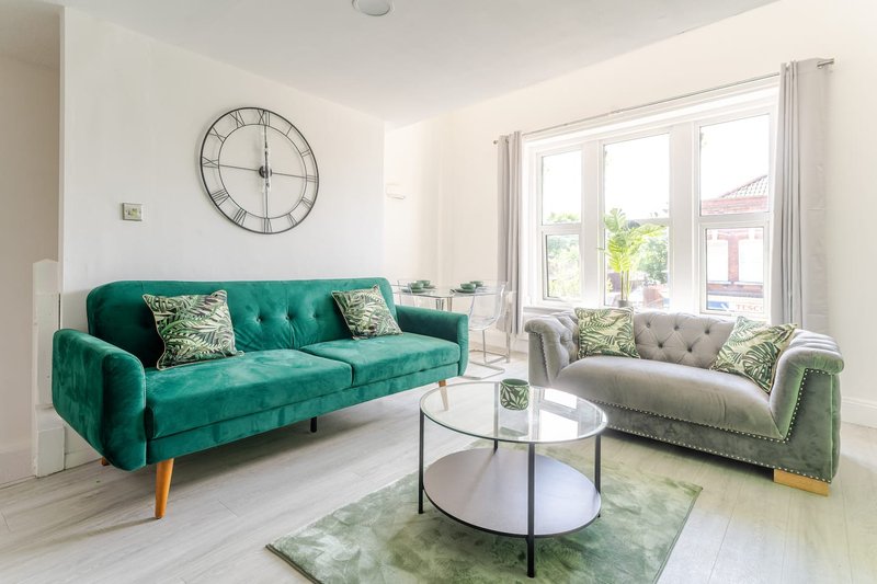 Bright living room with teal velvet sofa, light grey armchair, round glass coffee table and large windows