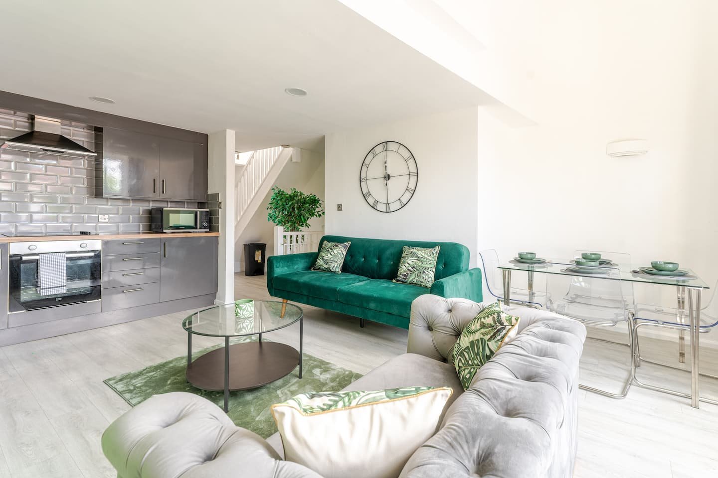 Open-plan living room and kitchen with green velvet sofa, gray seating, and modern furnishings