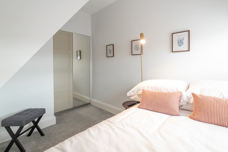 Bright modern bedroom with double bed, orange gingham pillows, ensuite door, and framed wall art