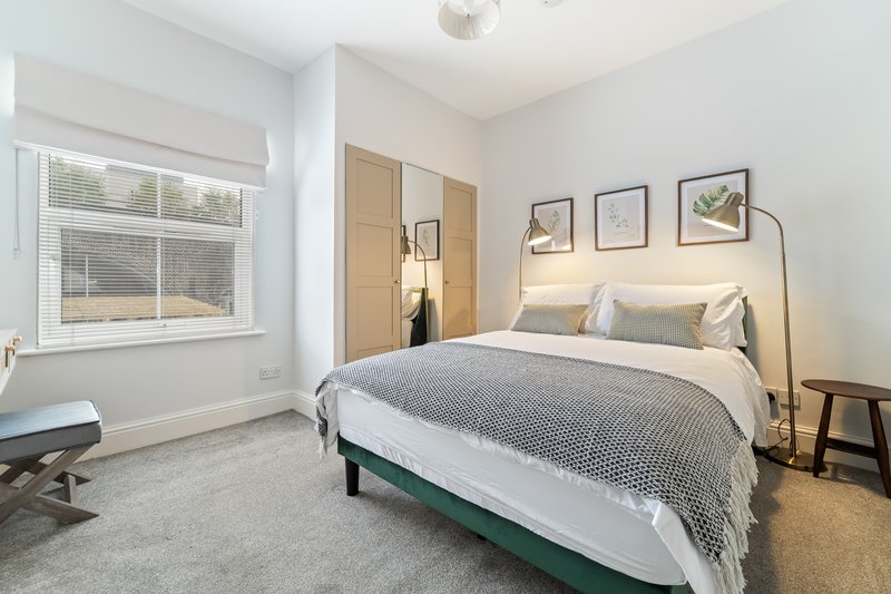 Bright modern bedroom with double bed, grey carpet, window seat and arc floor lamp