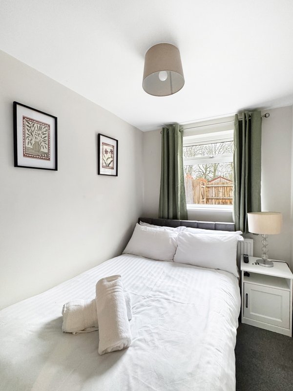 Bedroom with double bed, white bedding, green curtains, framed wall art, and ceiling light