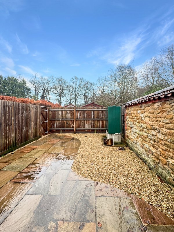 Backyard garden with paved patio, gravel area, wooden fencing and bare trees