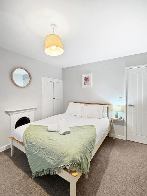 Bright bedroom with white wooden bed, green throw, yellow ceiling light and mirror
