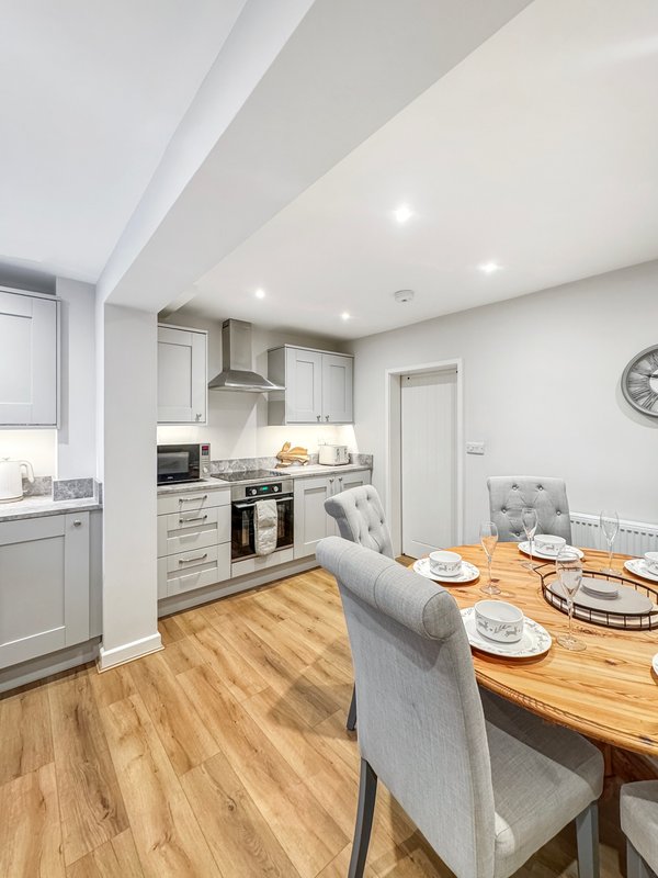 Open-plan kitchen and dining area with wooden table, grey chairs, white cabinetry and recessed lighting