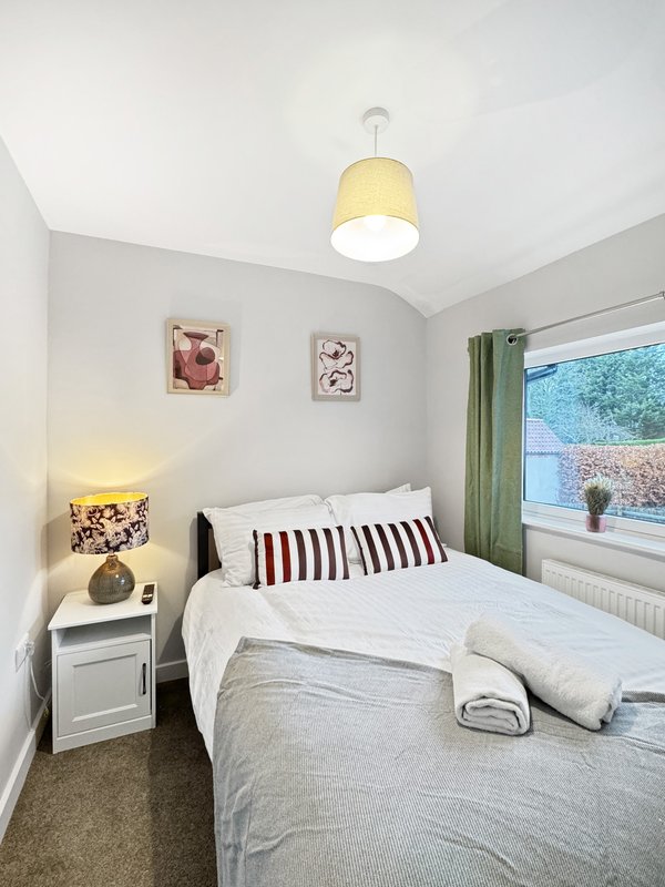 Bright bedroom with double bed, striped pillows, pendant light and window view