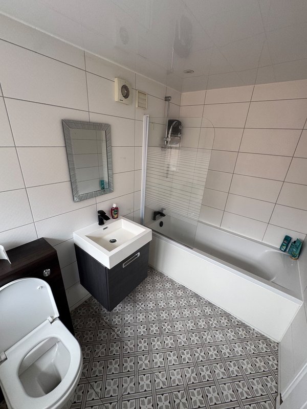 Modern bathroom with white tile walls, patterned floor tiles, vanity sink and bathtub