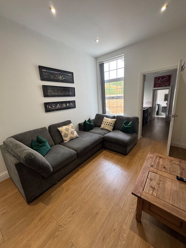 Modern living room with grey L-shaped sofa, wooden floor, wall art and large window