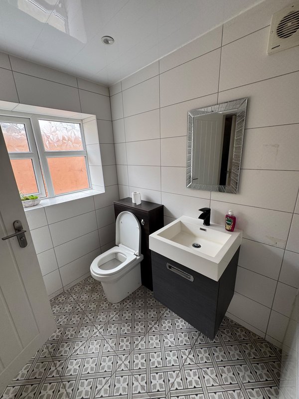 Modern bathroom with toilet, sink vanity, mirror and tiled walls