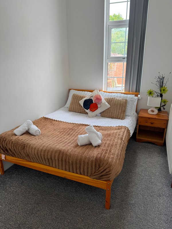 Bright bedroom with double bed, brown quilted bedding, wooden frame and nightstand