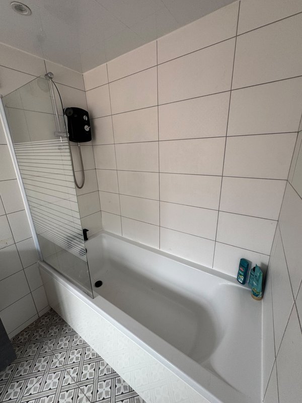 Clean bathroom with white subway tiles, bathtub with glass shower screen and toiletries