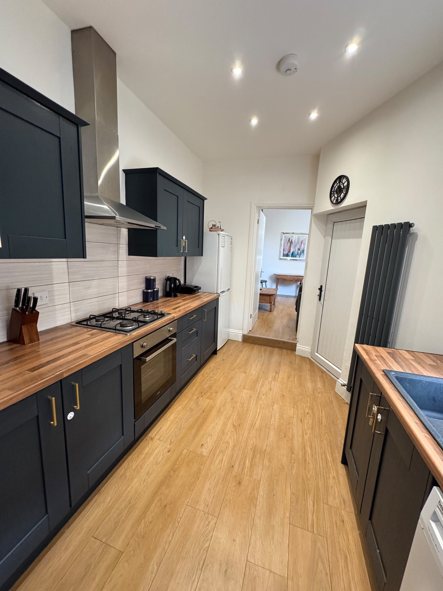 Modern galley kitchen with dark cabinetry, wooden countertops, stainless steel appliances and white tile backsplash