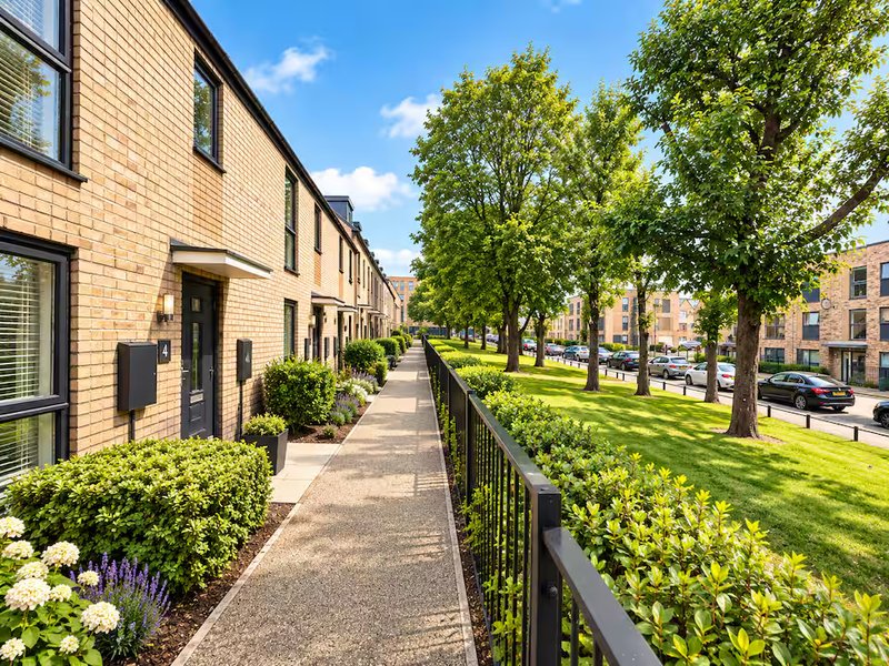 Brick townhouse exterior with paved pathway, manicured gardens, green trees and street view