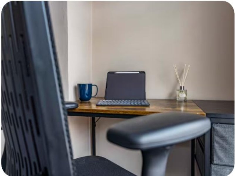 Home office desk with laptop, blue mug, reed diffuser and black office chair