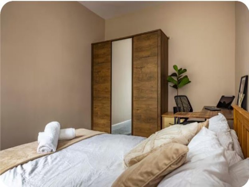 Bedroom with double bed, wooden wardrobe, desk area and potted plant