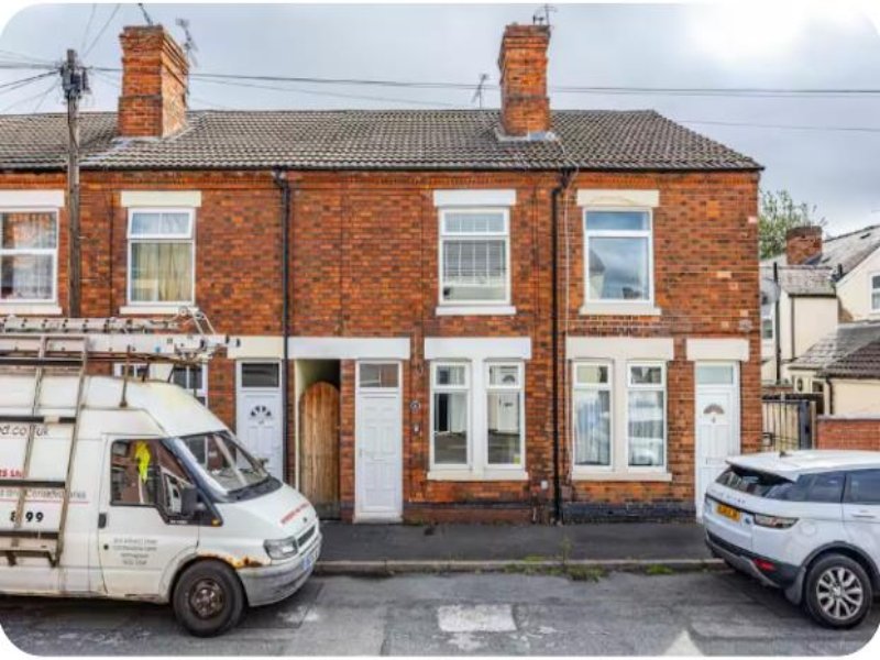 Red brick terraced house with white windows, two chimneys, and parked vehicles on street